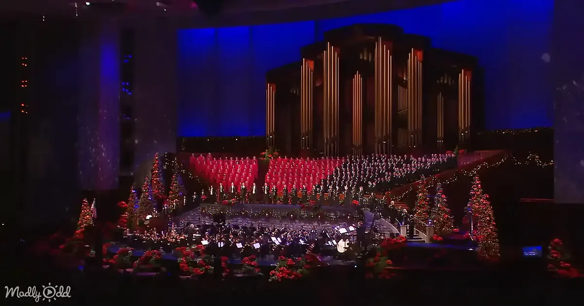 A grand Christmas concert scene with a large choir in red and a festive orchestra on stage.