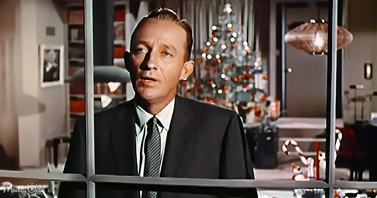 A man in a suit stands in front of a Christmas tree, looking to the side.