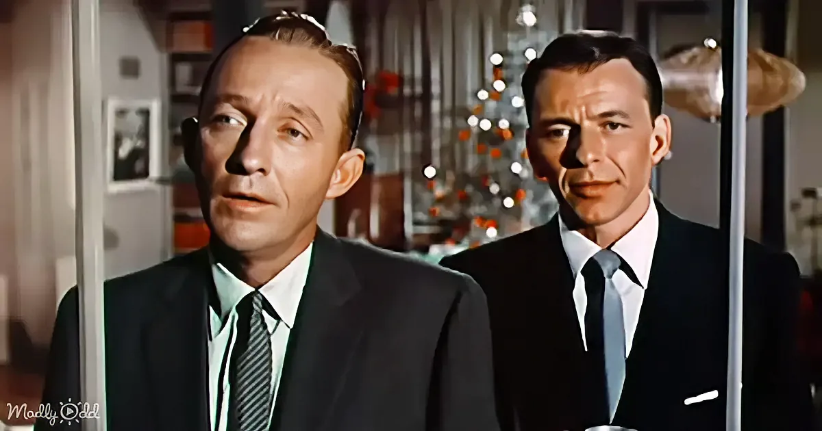 Two men in suits stand indoors, one with a Christmas tree in the background.