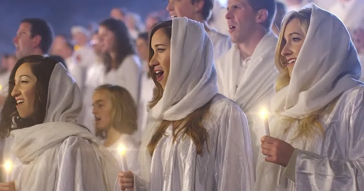 A group of people in white robes and hoods, holding candles, singing in a choir.
