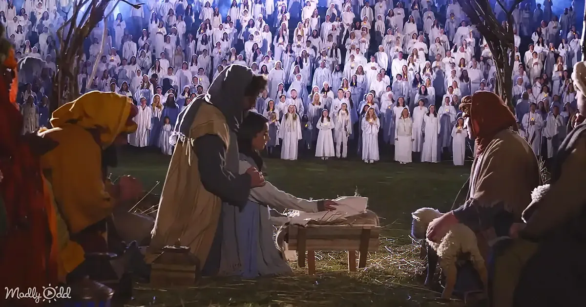 Mary and Joseph with baby Jesus surrounded by shepherds and a crowd in white robes holding candles.