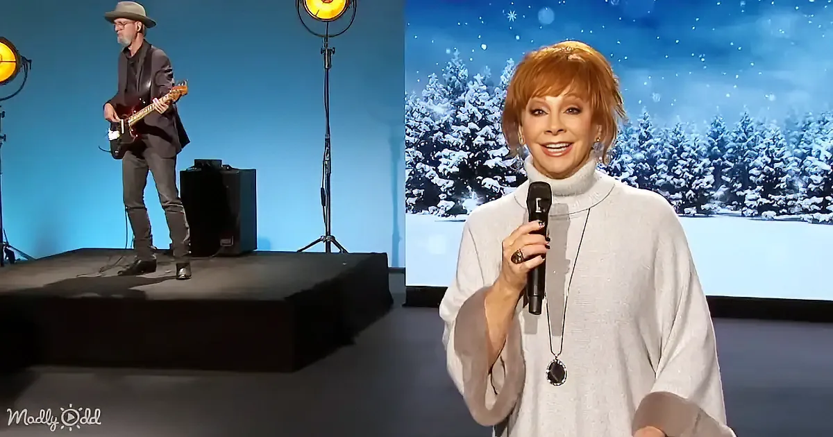 Woman with microphone smiles in snowy backdrop, man plays guitar on stage.