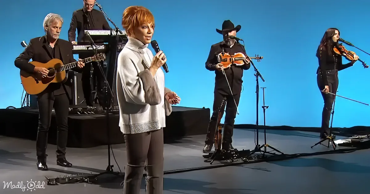 A woman in a white sweater sings into a microphone on stage with a band.
