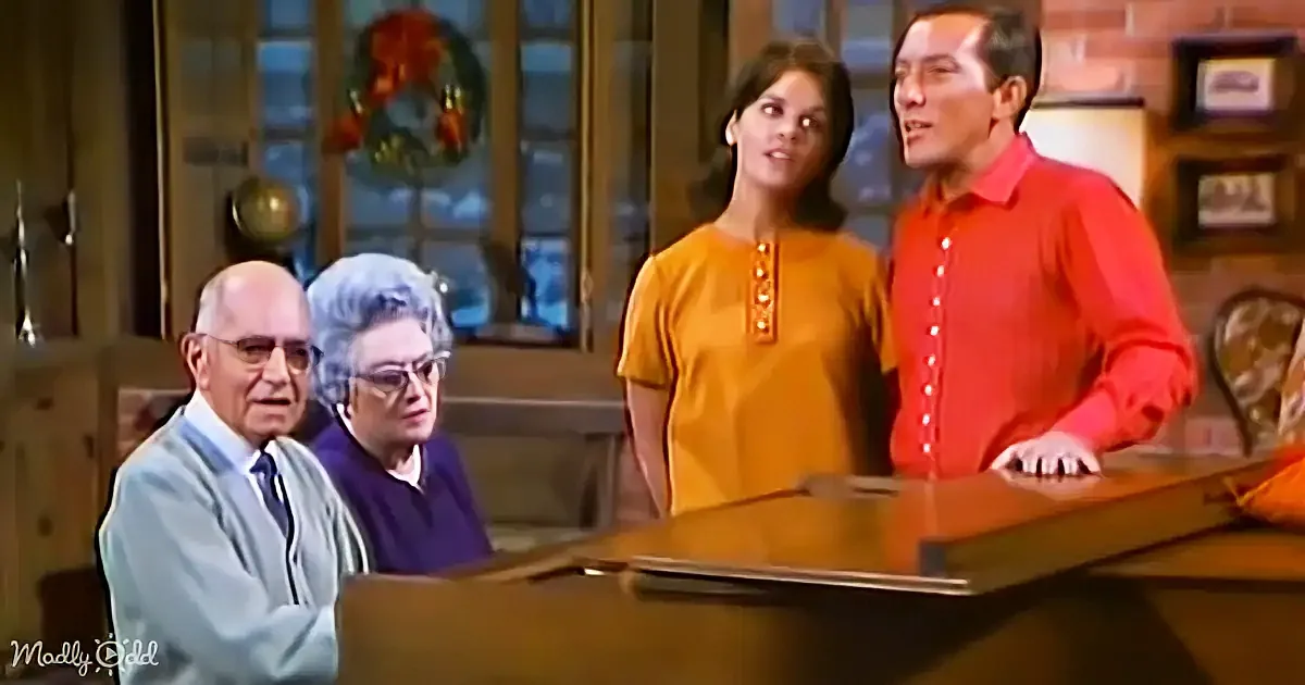 A family scene with a man in a red shirt and a woman in a yellow top standing, while an older couple sits at a piano.