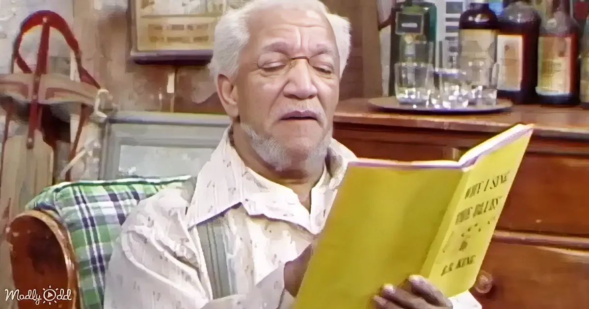 An elderly man with white hair reads a yellow book in a plaid chair.
