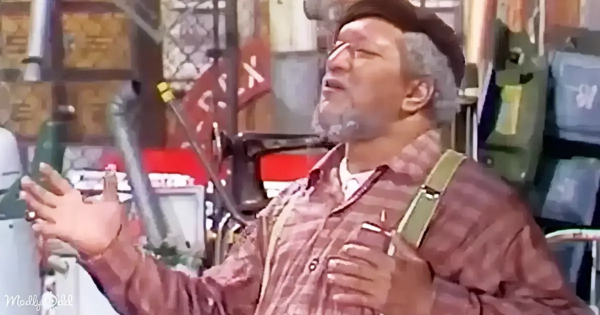 A man in a plaid shirt and suspenders is singing passionately with his eyes closed and hands raised.