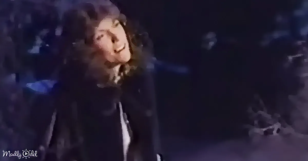 A person in a dark jacket smiles while standing on a dimly lit stage.