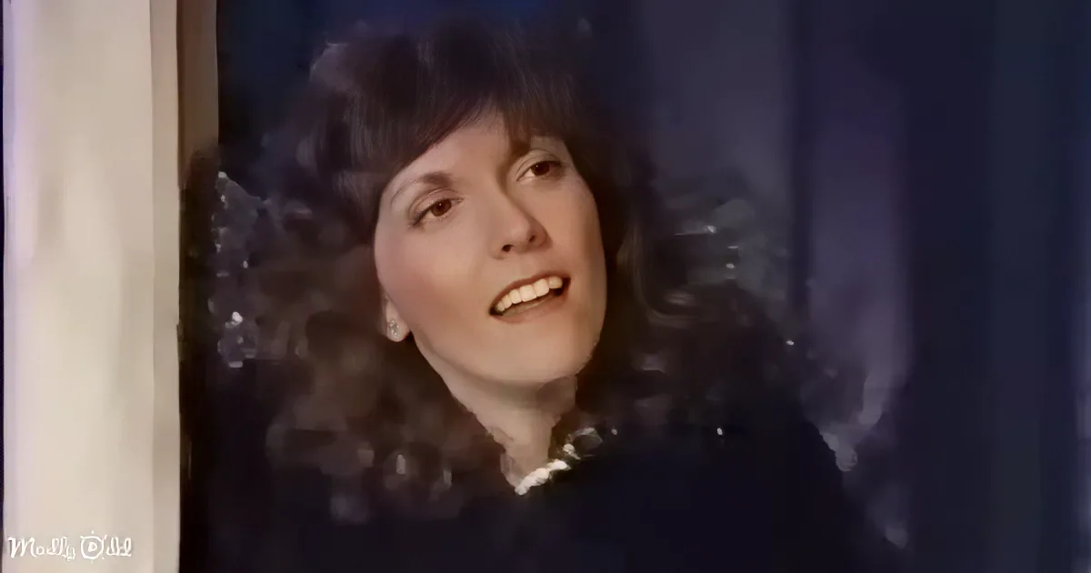 A woman with curly hair and a dark outfit is smiling, looking upwards.