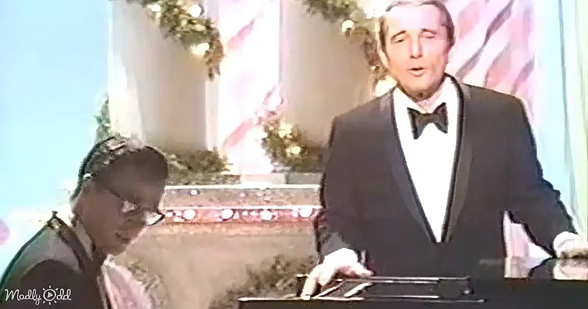 A man in a tuxedo stands at a piano, while another person plays, both in a festive setting.