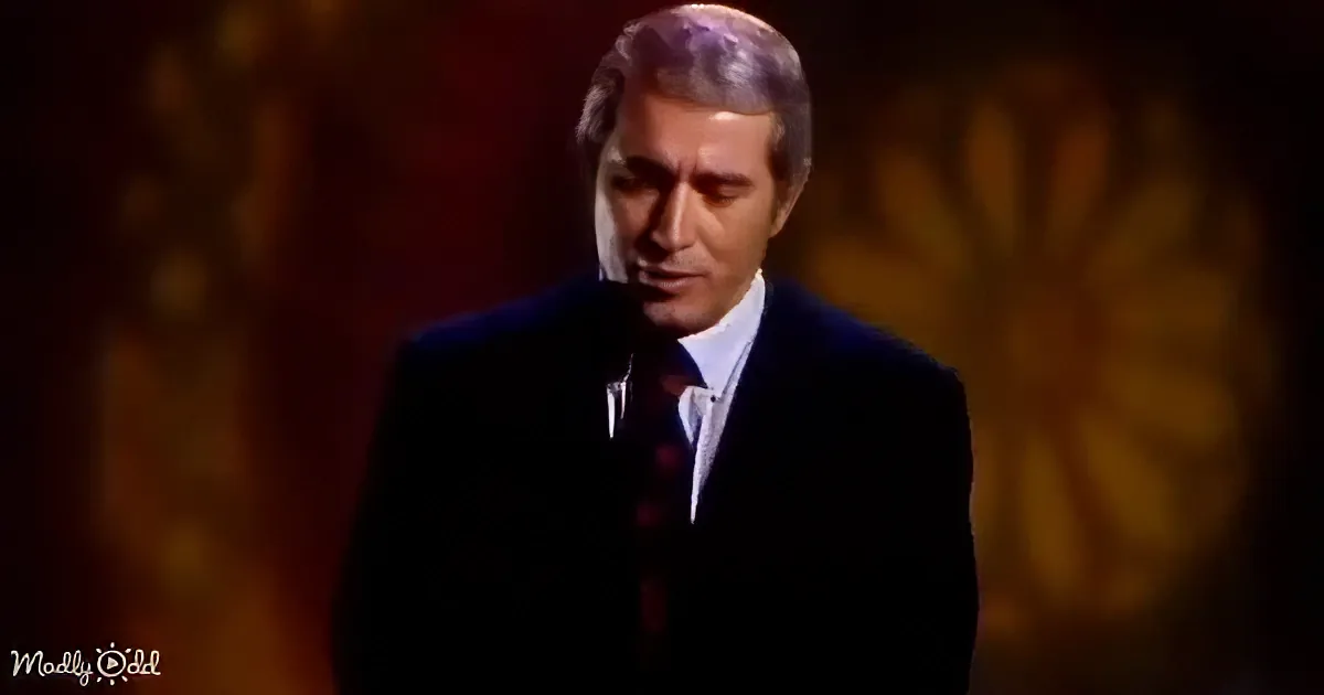 A man in a dark suit and tie stands against a blurred, warm-toned background.