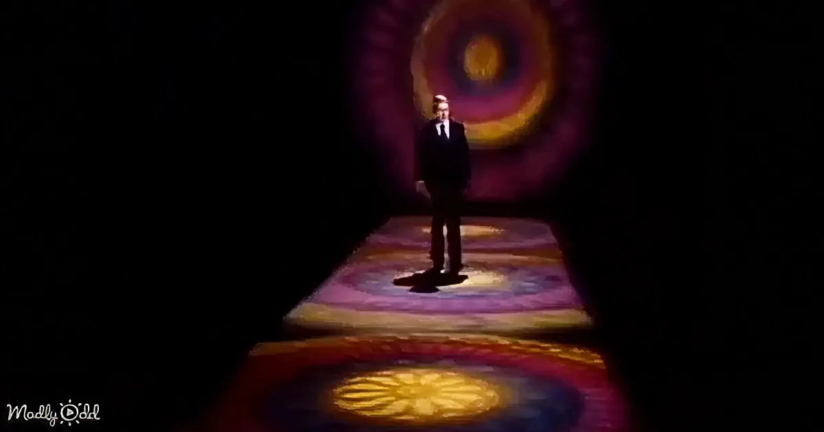 A man in a suit stands on a colorful, patterned stage with a circular design behind him.