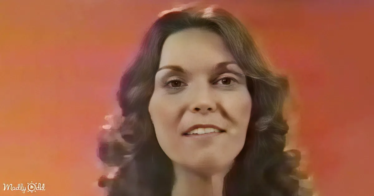 A woman with long, dark, curly hair is shown against a gradient orange-red background.