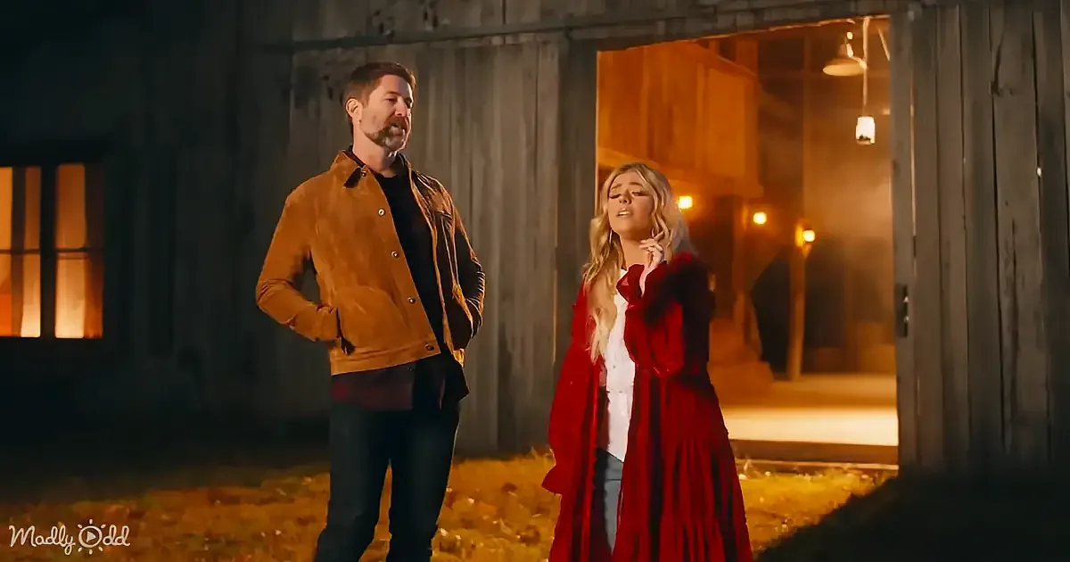 A man in a brown jacket and a woman in a red coat stand outside a barn at night.