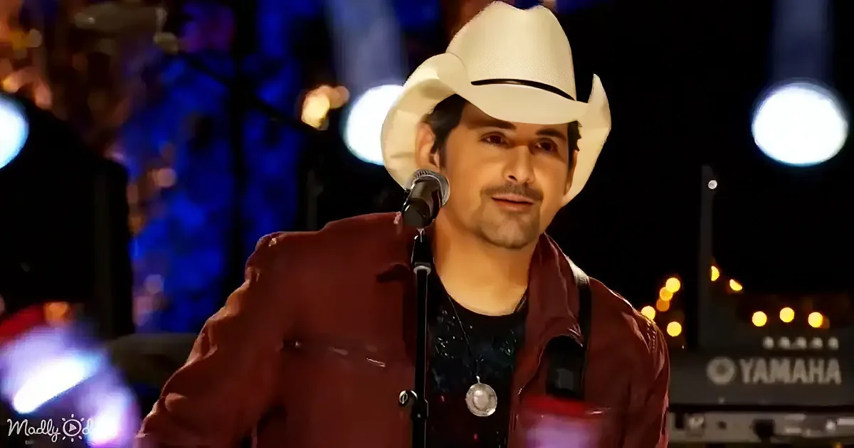 A man in a white cowboy hat and red jacket sings into a microphone on stage.