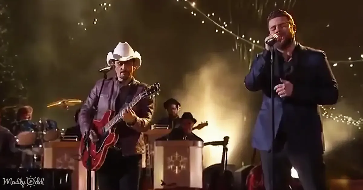 A man in a white cowboy hat plays guitar while another sings into a microphone on stage.