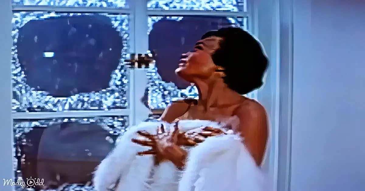 A woman in a white dress is singing passionately, holding a microphone, with a snowy window in the background.