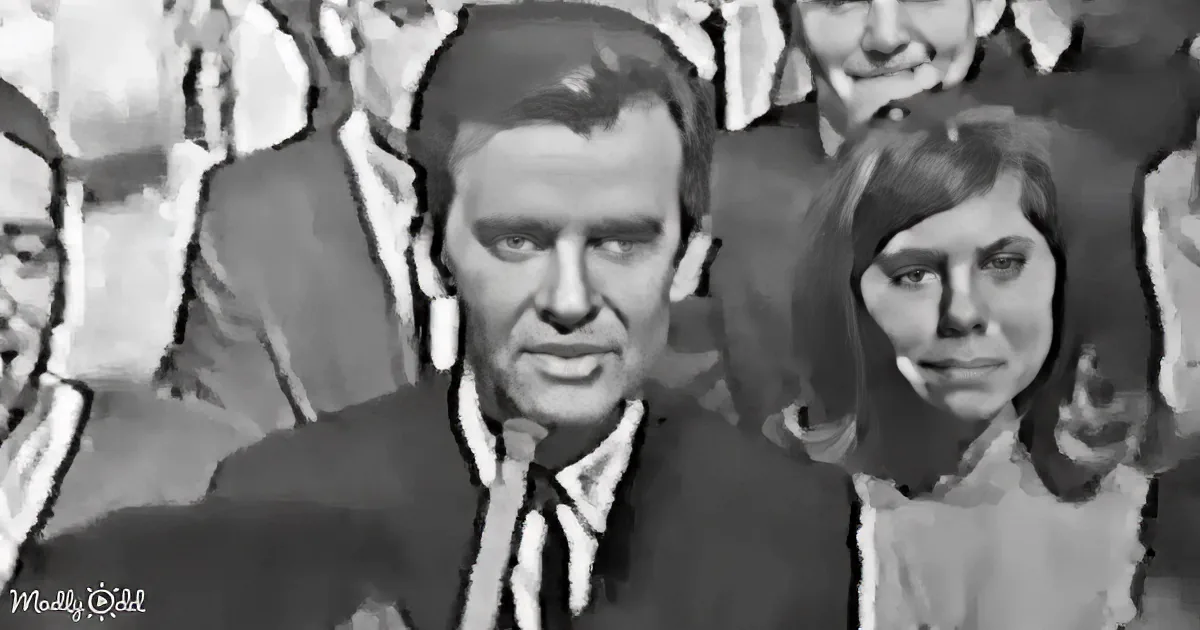 A man in a suit and tie is speaking, surrounded by people in formal attire, in a black-and-white setting.