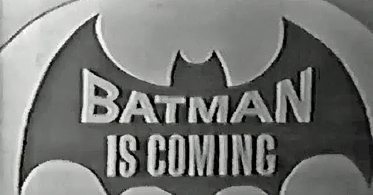 A man in a suit and tie speaks into a microphone, next to a comic-style image of Batman with the word "SOCK!"