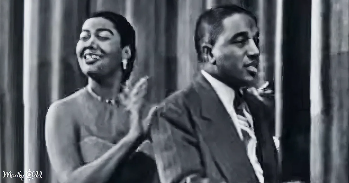 A smiling woman clapping, a man singing, both in front of a curtain backdrop.