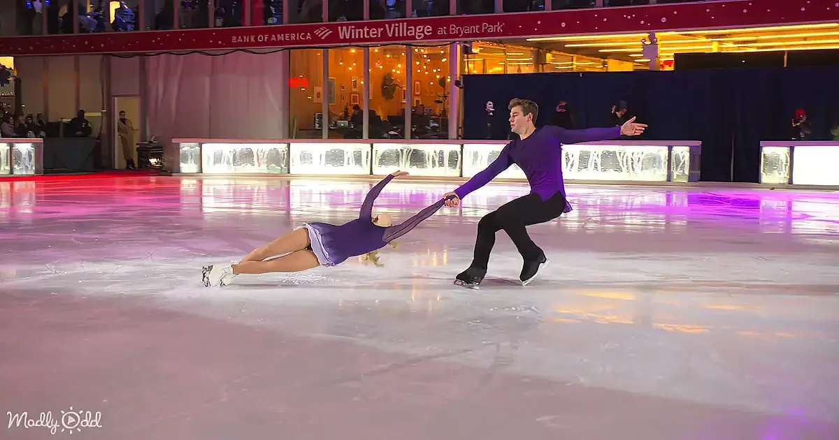 A man and woman are ice skating, with the woman sliding while the man holds her hand.