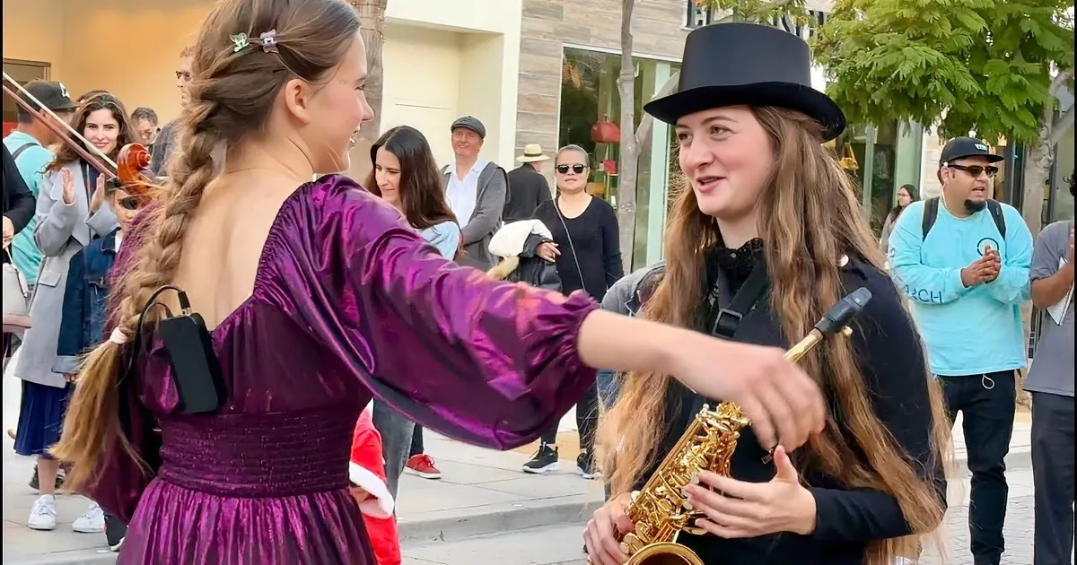 A girl in a purple dress plays violin while a boy in a top hat plays saxophone in a bustling public space.