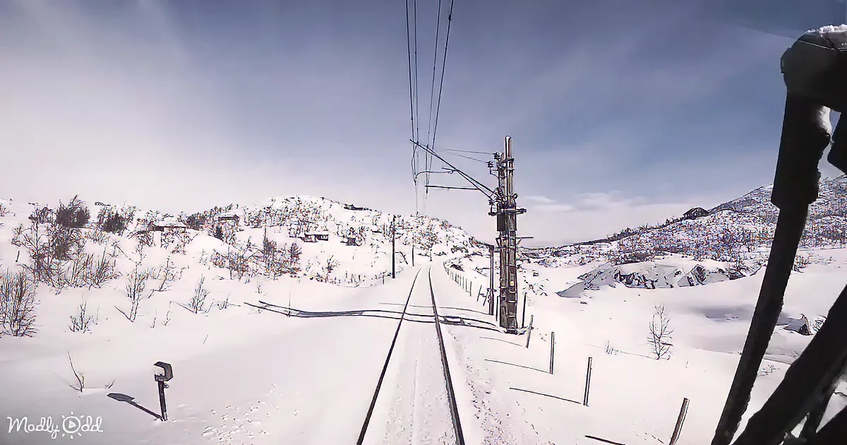 A snowy railway track stretches through a mountainous landscape under a clear sky.