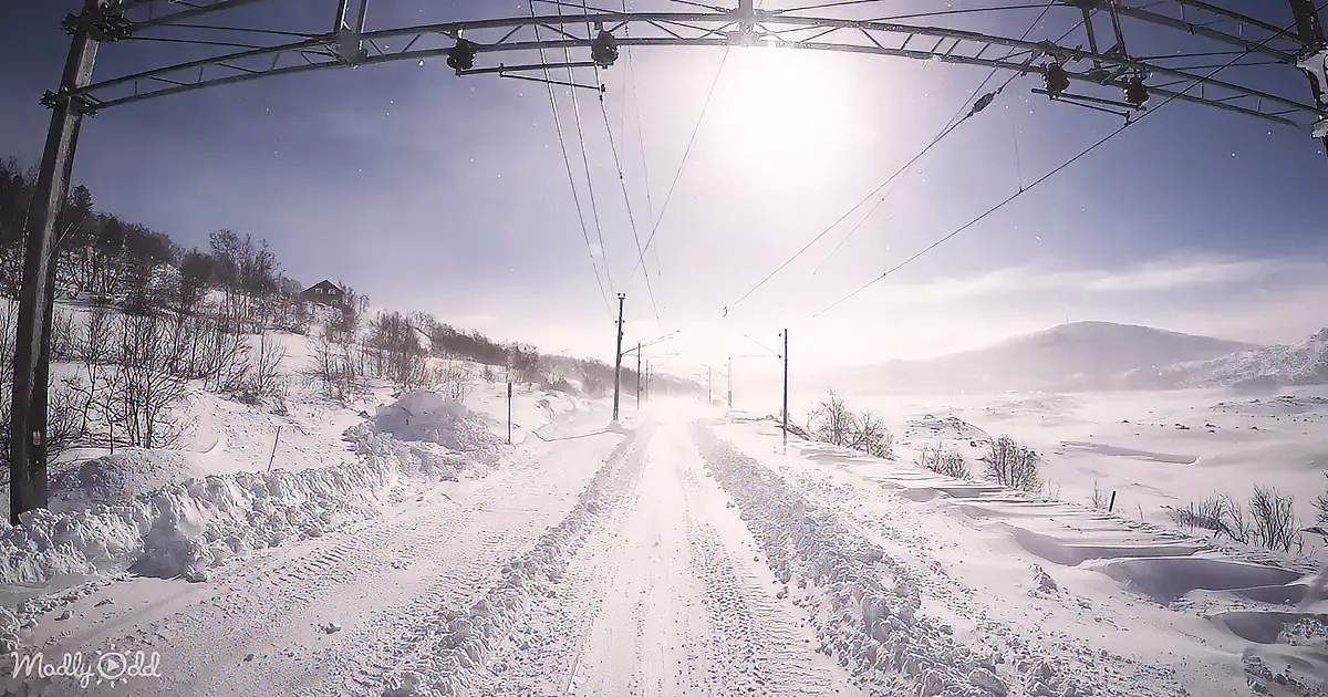 A snowy road under bright sunlight, with power lines overhead and snow-covered hills in the background.