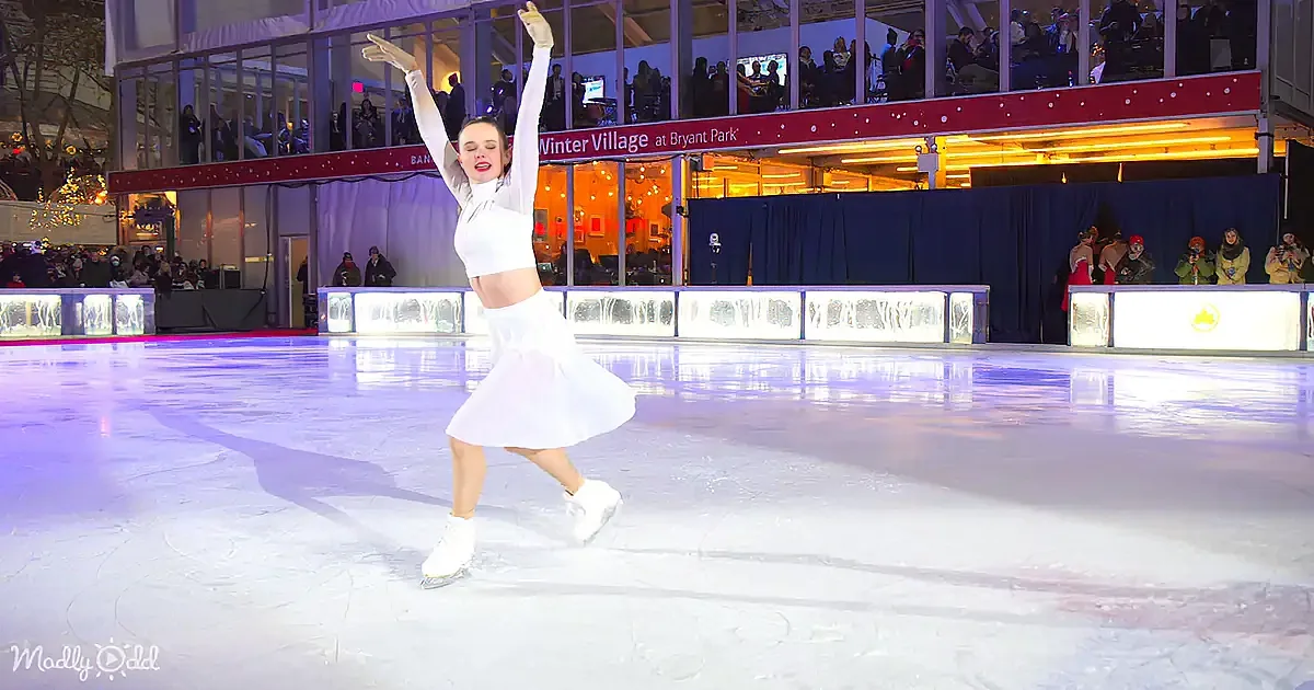 A figure skater in white performs gracefully on an ice rink at the Winter Village in Bryant Park.