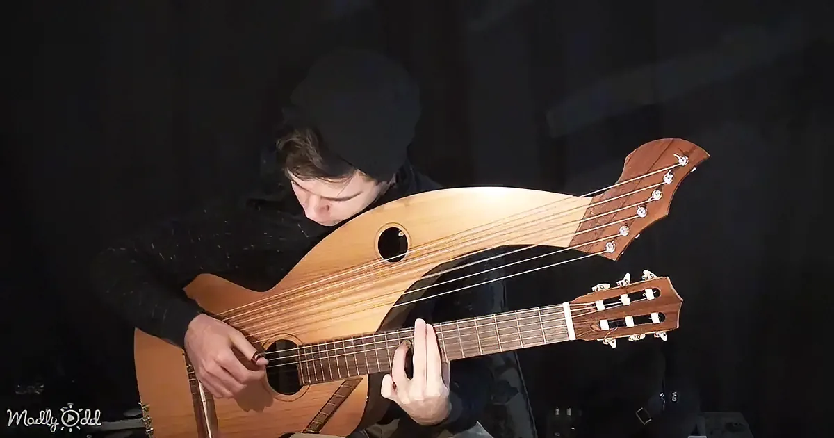 A person plays a unique stringed instrument with a fish-like body and six strings.