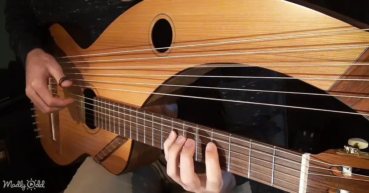 A person plays a wooden stringed instrument with a circular sound hole and multiple strings.