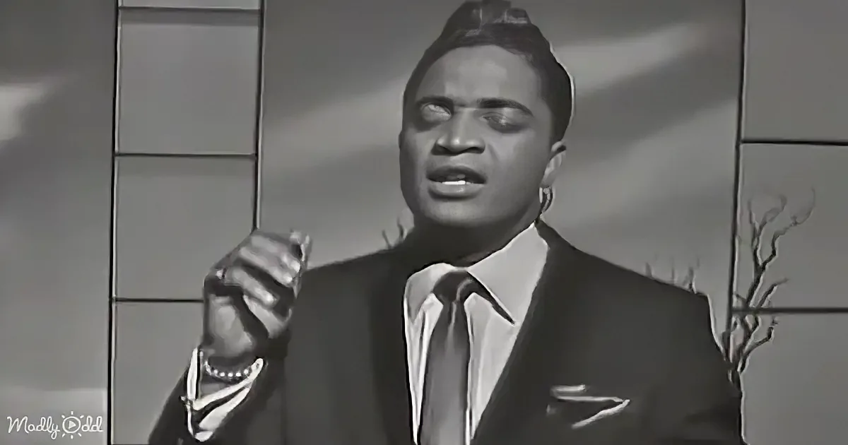 A man in a suit and tie is singing passionately with his eyes closed, holding a microphone.