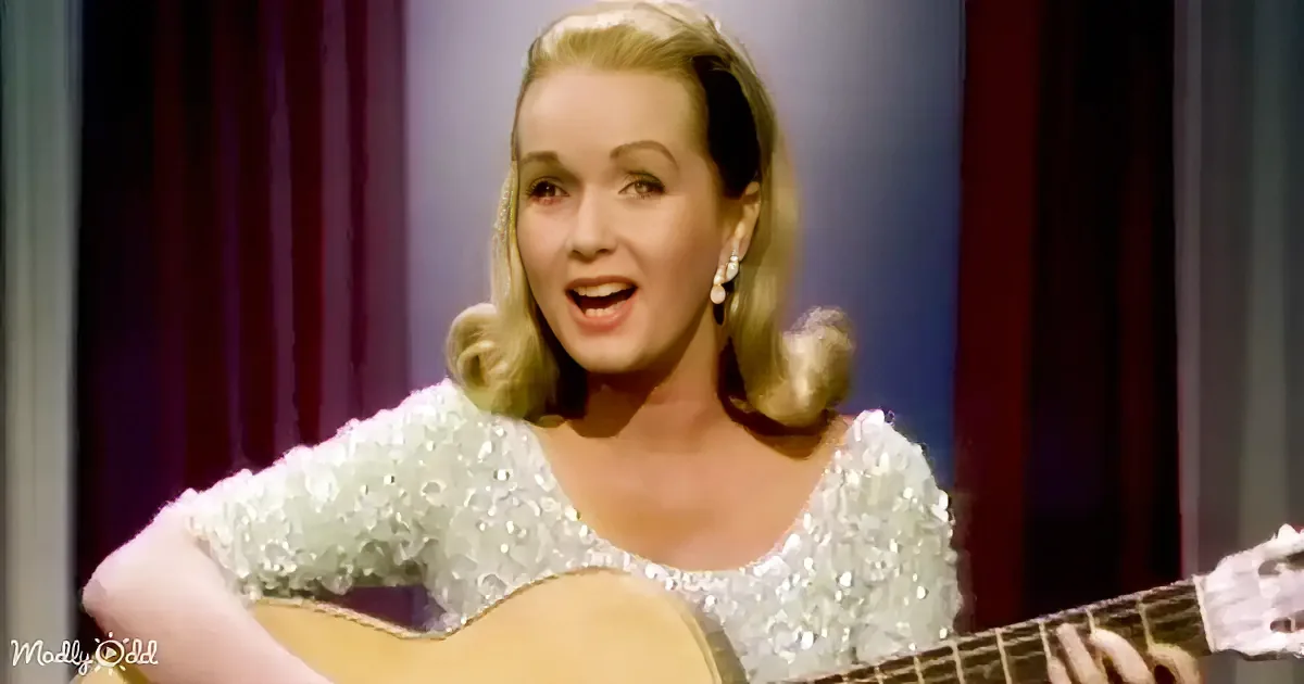 A woman in a sparkly white dress plays an acoustic guitar on stage.