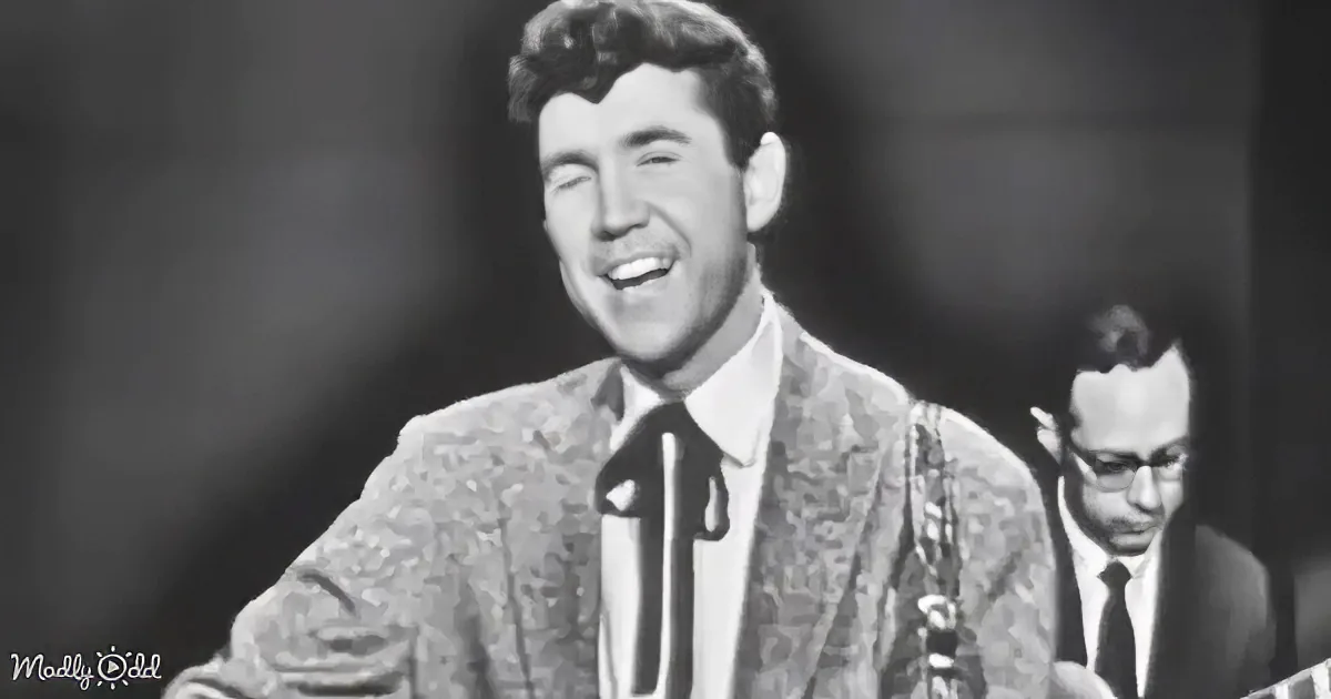 A man in a patterned suit and bow tie smiles widely, with another person in the background.