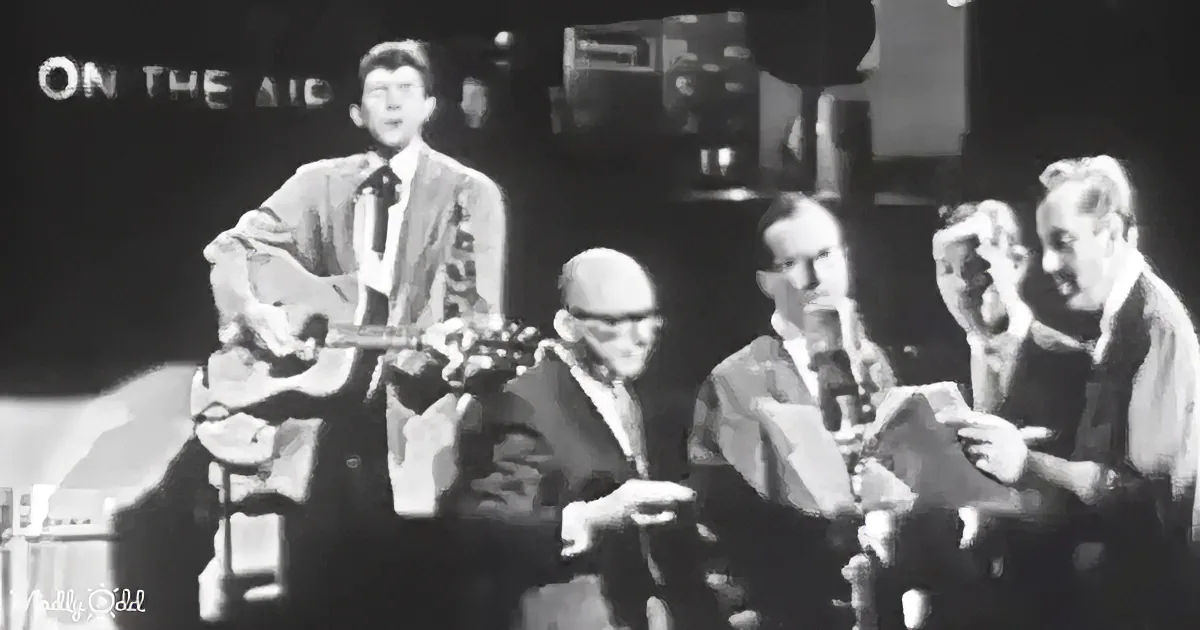 A man plays guitar while seated musicians read sheet music in a radio studio.
