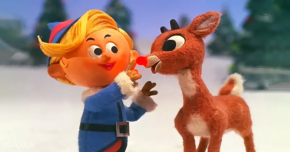 A cheerful elf in a blue outfit interacts with a red-nosed reindeer in a snowy setting.