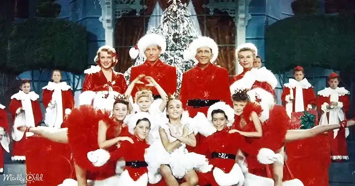 A festive group in red and white costumes, posing joyfully in front of a Christmas tree backdrop.