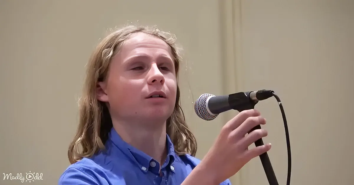 A person in a blue shirt holds a microphone, appearing to speak or sing.