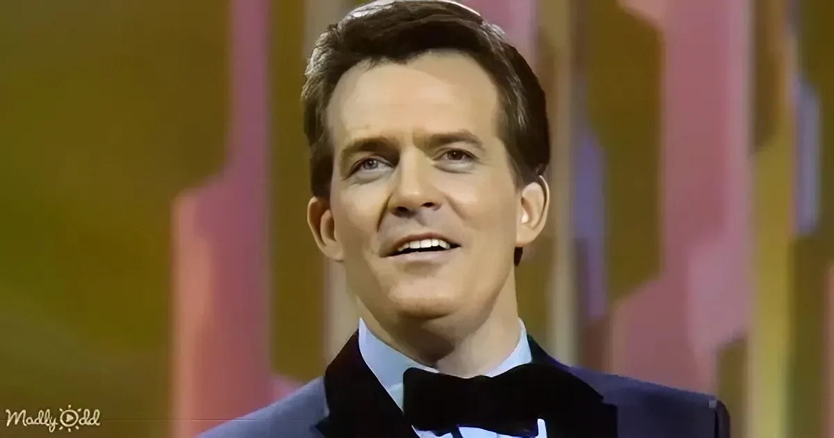 A man in a tuxedo with a bow tie smiles against a colorful, blurred background.