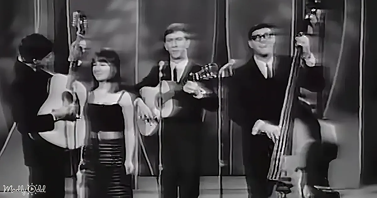 A band performs on stage with a female singer, two guitarists, and a bassist.