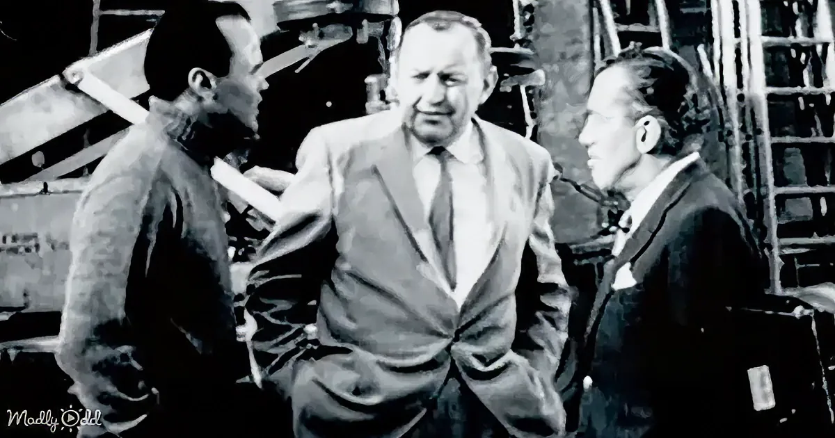 A man in a suit and tie stands between two others, one holding a book, in a dimly lit setting.
