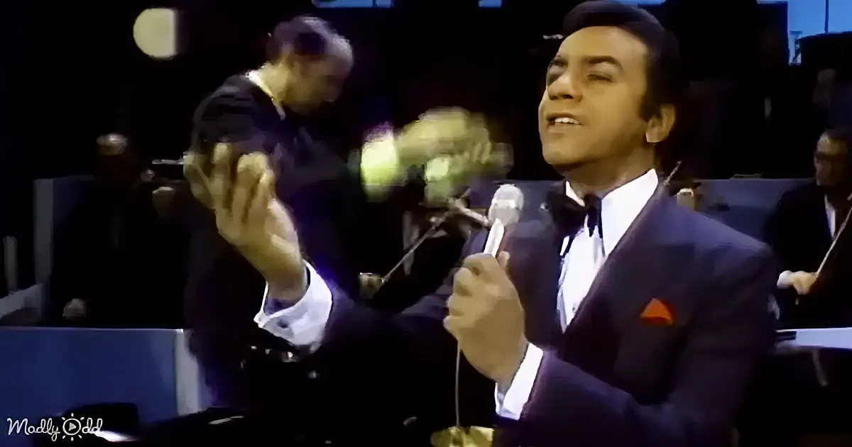A man in a suit sings into a microphone, gesturing with his other hand.