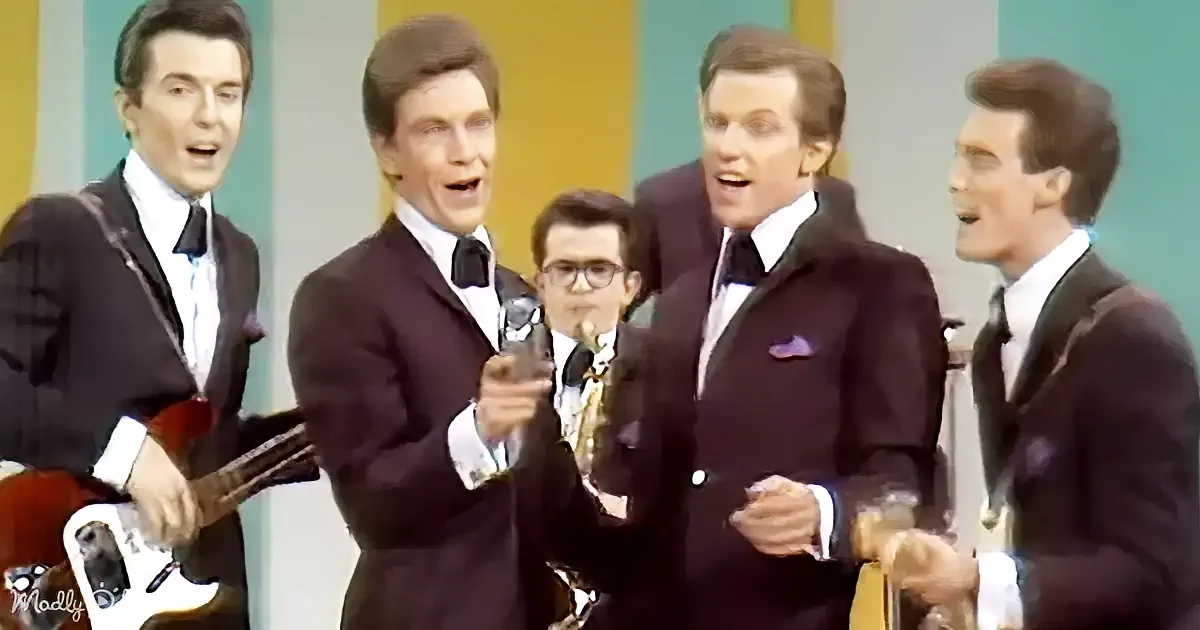 A group of men in suits sing and play instruments on a stage with colorful stripes.