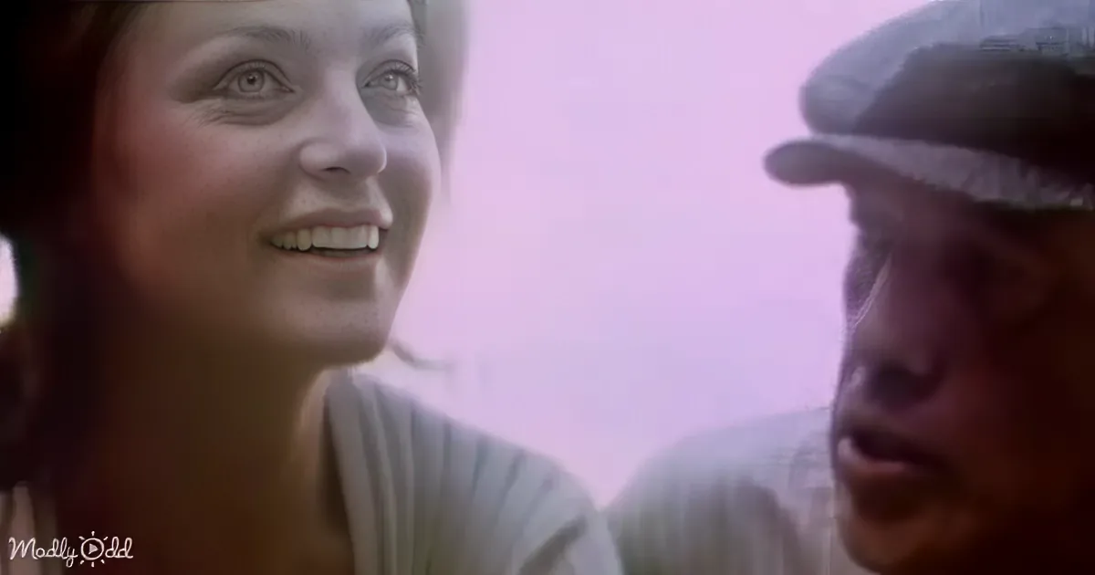 A woman with a warm smile and a man in a cap are shown in a close-up, possibly in a film scene.