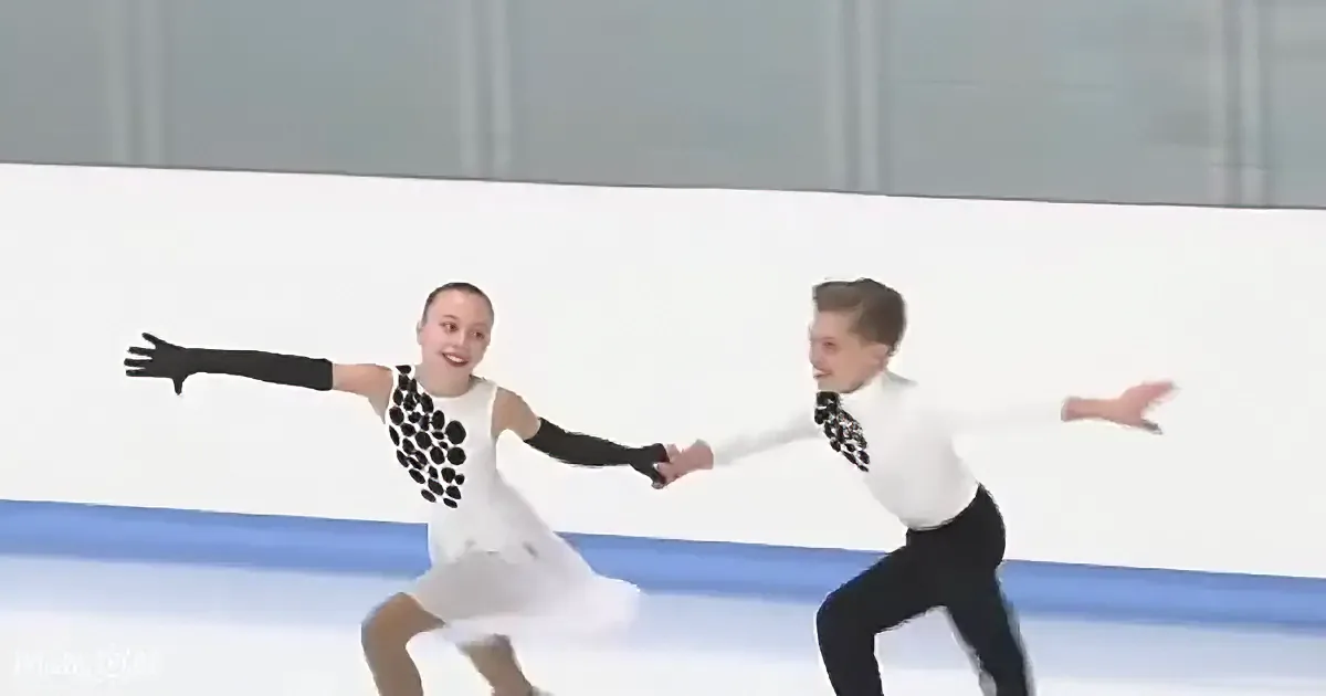 A figure skating pair in white and black costumes performs a synchronized move on the ice.