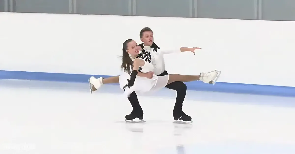 Two figure skaters in white and black costumes perform a synchronized move on ice.