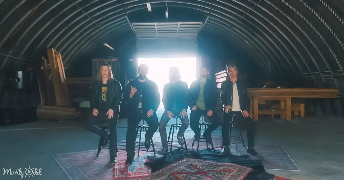 Five individuals sit on stools in a dimly lit, industrial space with a patterned rug and a bright light source in the...