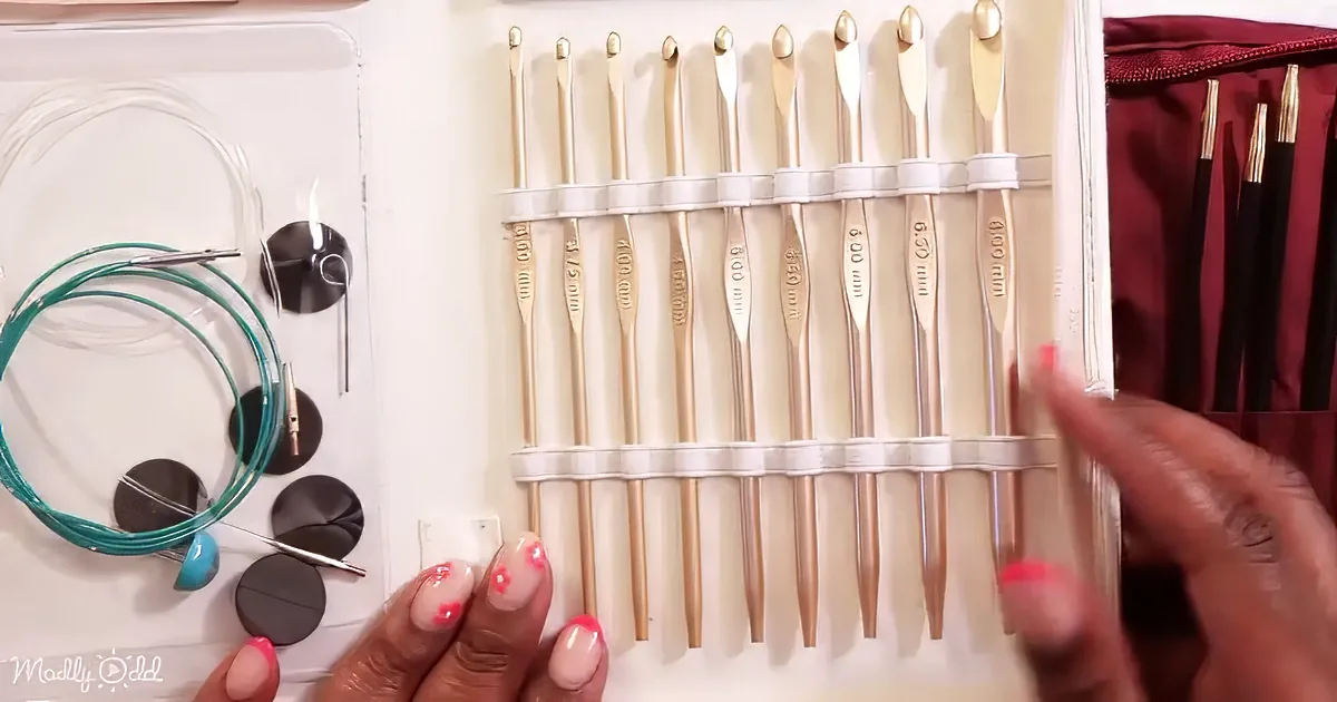 A hand points to a set of crochet hooks in a case, with various sizes and a turquoise wire on the left.