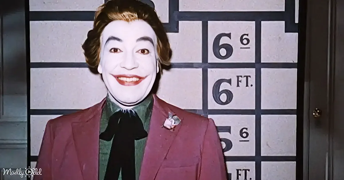 A person in a Joker costume stands in front of a height chart, wearing a red suit and green shirt.