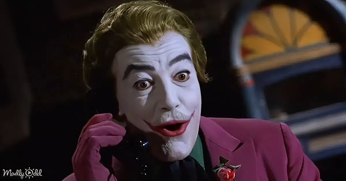 A person in a Joker costume with white face paint, red lips, and a pink suit, holding a phone to their ear.