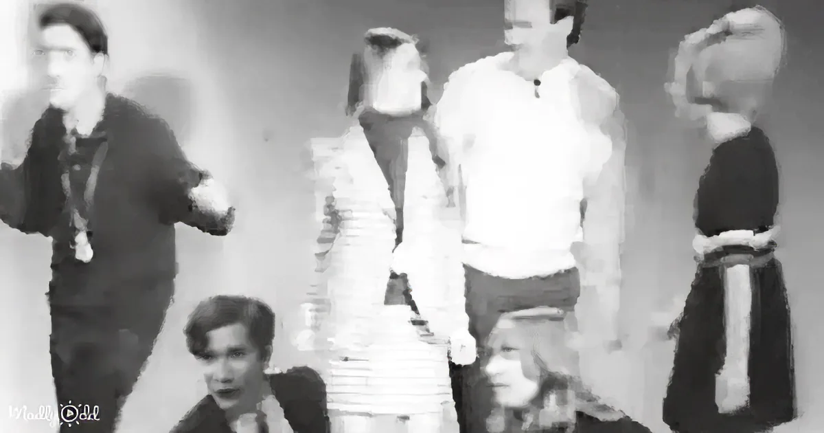 A man in a dark shirt gestures while standing with others in a dimly lit room.
